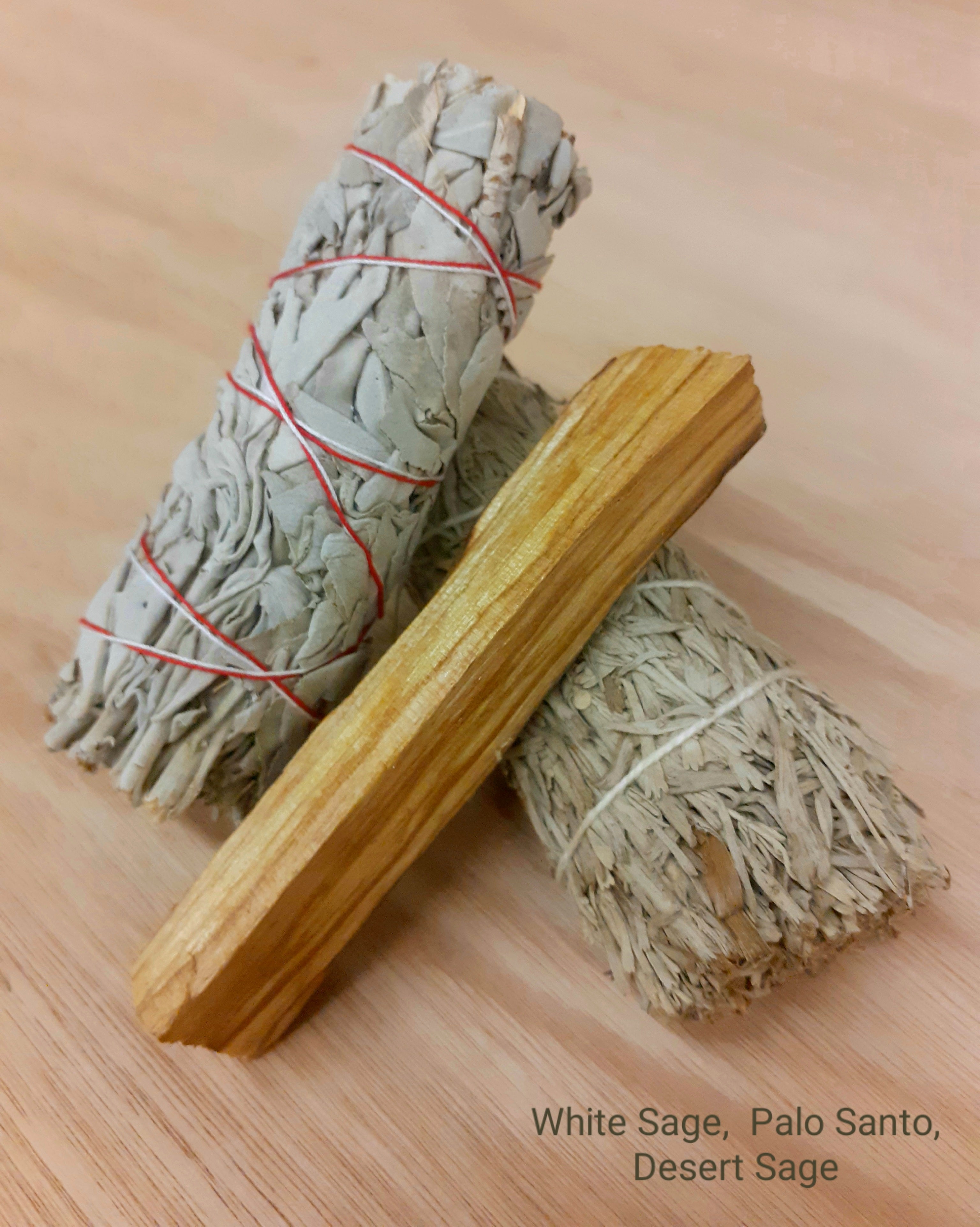 An assortment of 4-inch cleansing items, featuring a fragrant white sage smudge stick, a blue sage stick, and a natural Palo Santo wood piece, beautifully arranged for purifying and enhancing the energy of your space.